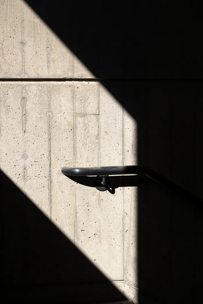 Raking sunlight across a rough concrete surface with a handrail shadow