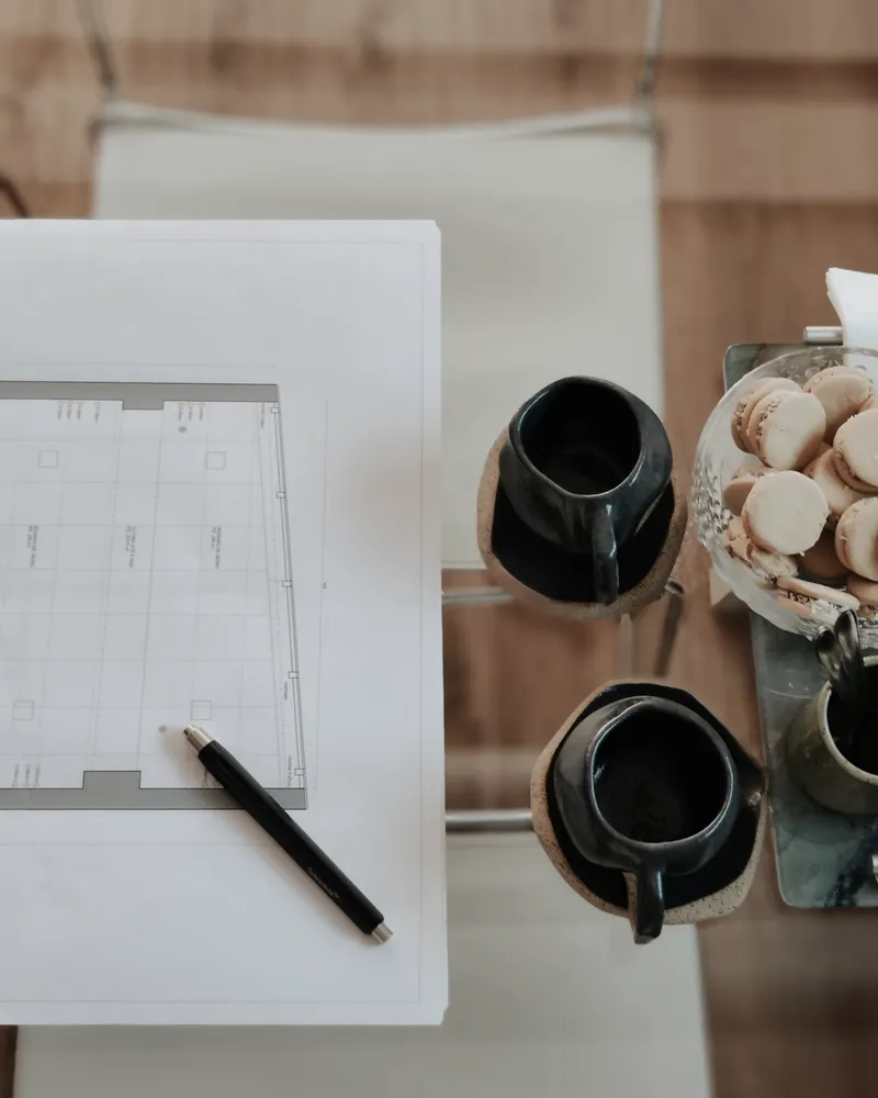 Architectural plans laid flat on a table beside two dark ceramic cups