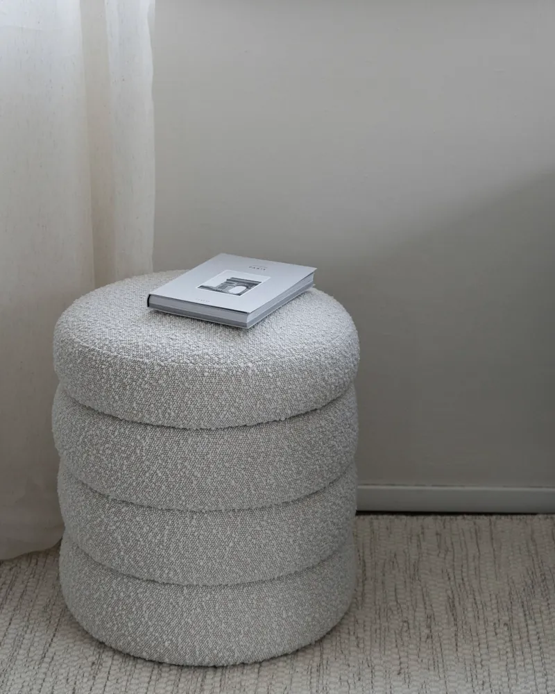 Close view of a cream boucle ottoman resting on a pale stone floor